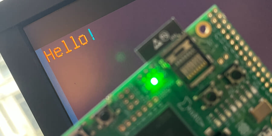 Photograph of ULX3S dev board showing 'Hello!' in Isle text mode on a widescreen monitor.